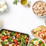 Ingredientes preparados para batch cooking saludable: huevos, patatas, verduras asadas y pollo desmenuzado sobre fondo claro